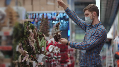 Shopping-in-pandemic-and-quarantine.-A-man-in-a-protective-mask-in-a-jewelry-store-and-garlands-with-toys-for-Christmas-trees-and-at-home.-Christmas-garlands-and-decor.
